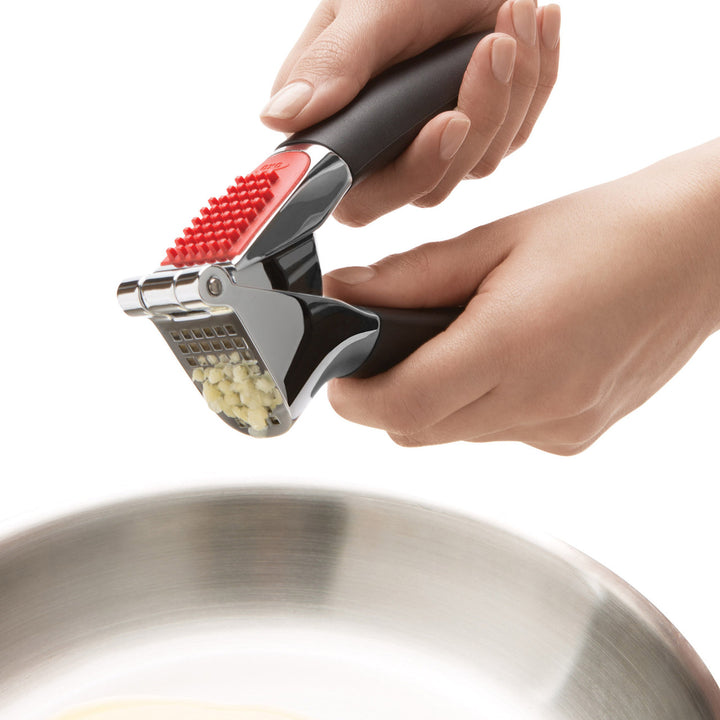 Hand using a garlic press to crush garlic over a frying pan on a white background