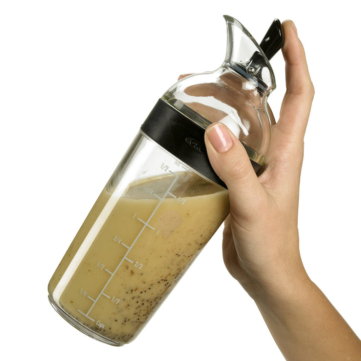 Hand holding a glass measuring container with a liquid mixture on a white background