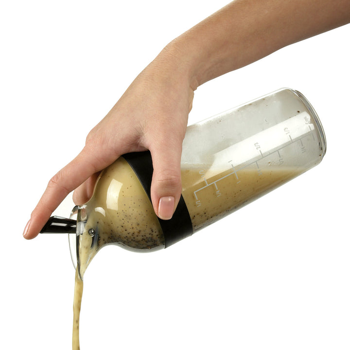 Hand pouring a liquid from a glass container with measurement markings on a white background