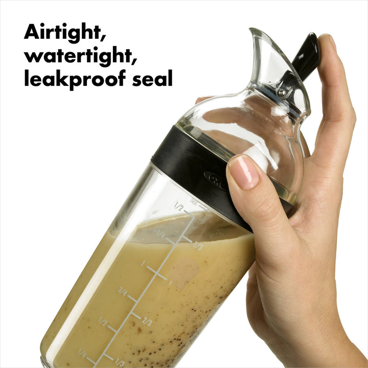 Glass carafe with airtight, watertight, leakproof seal held by a hand, with text &
