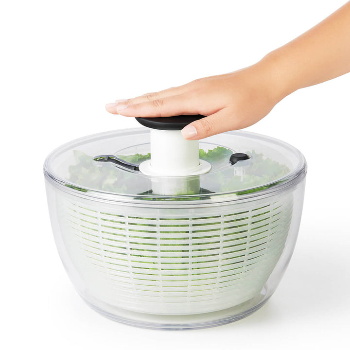 Hand using a salad spinner with lettuce on a white background