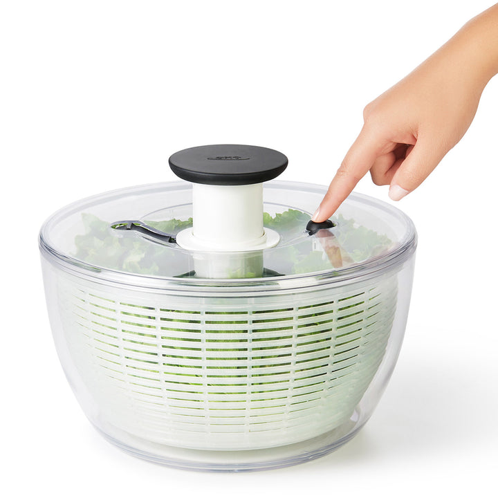 Hand using a salad spinner with lettuce on a white background