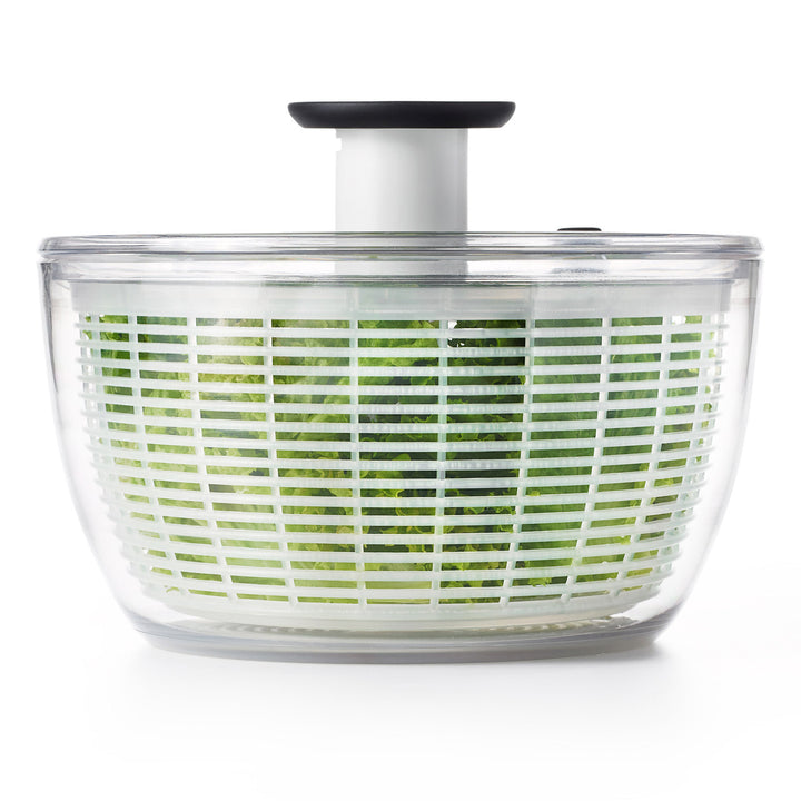 Clear salad spinner with green vegetables on a white background