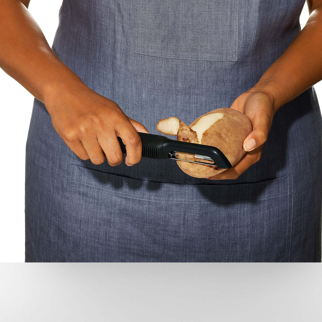 Person peeling a potato with a peeler against a white background