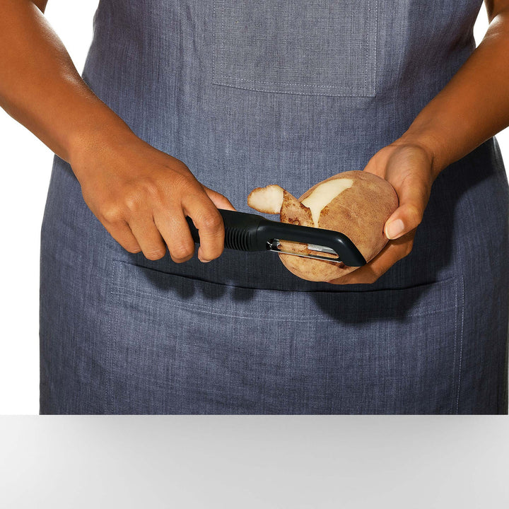 Person peeling a potato with a peeler against a white background
