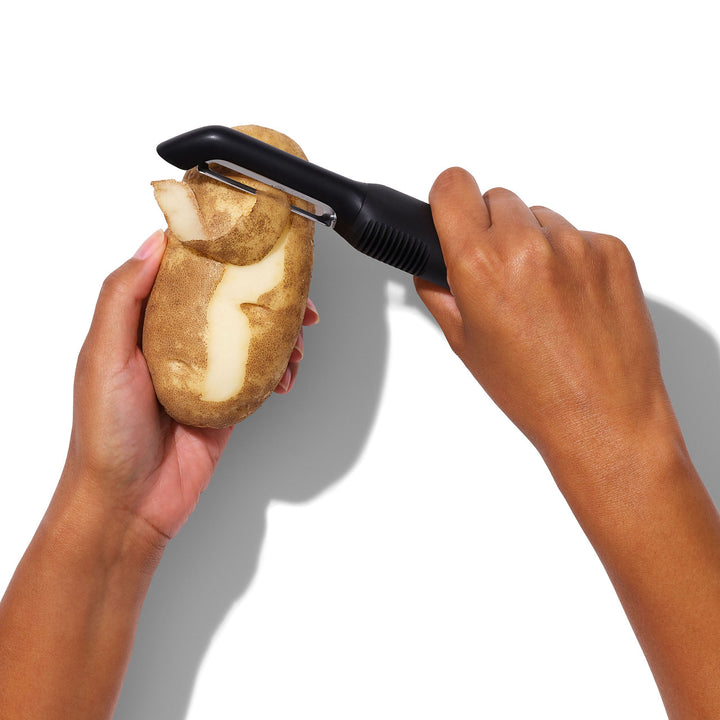 Person peeling a potato with a black peeler on a white background