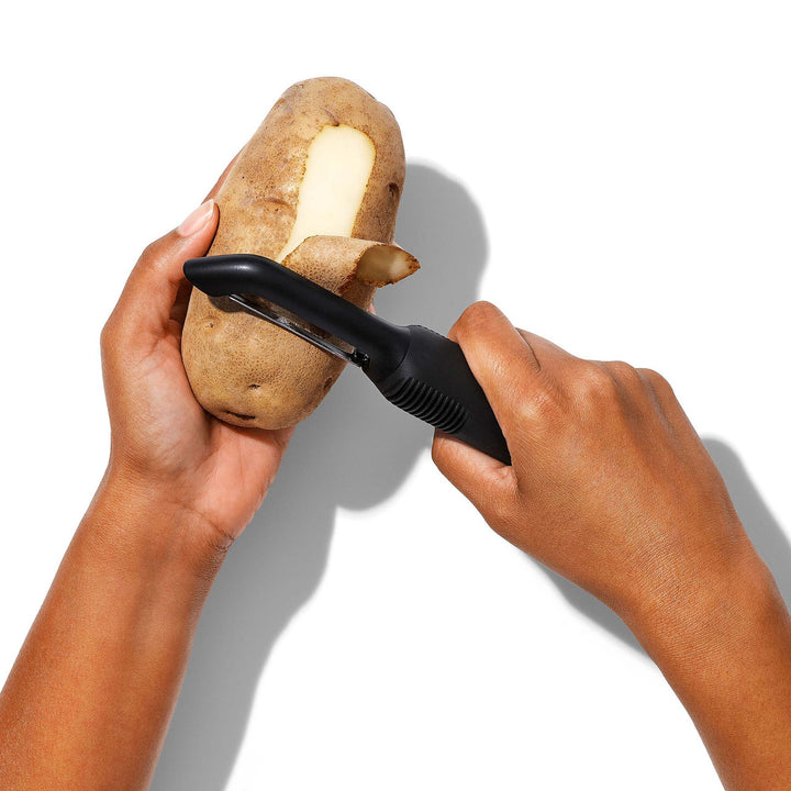 Person peeling a potato with a black peeler on a white background