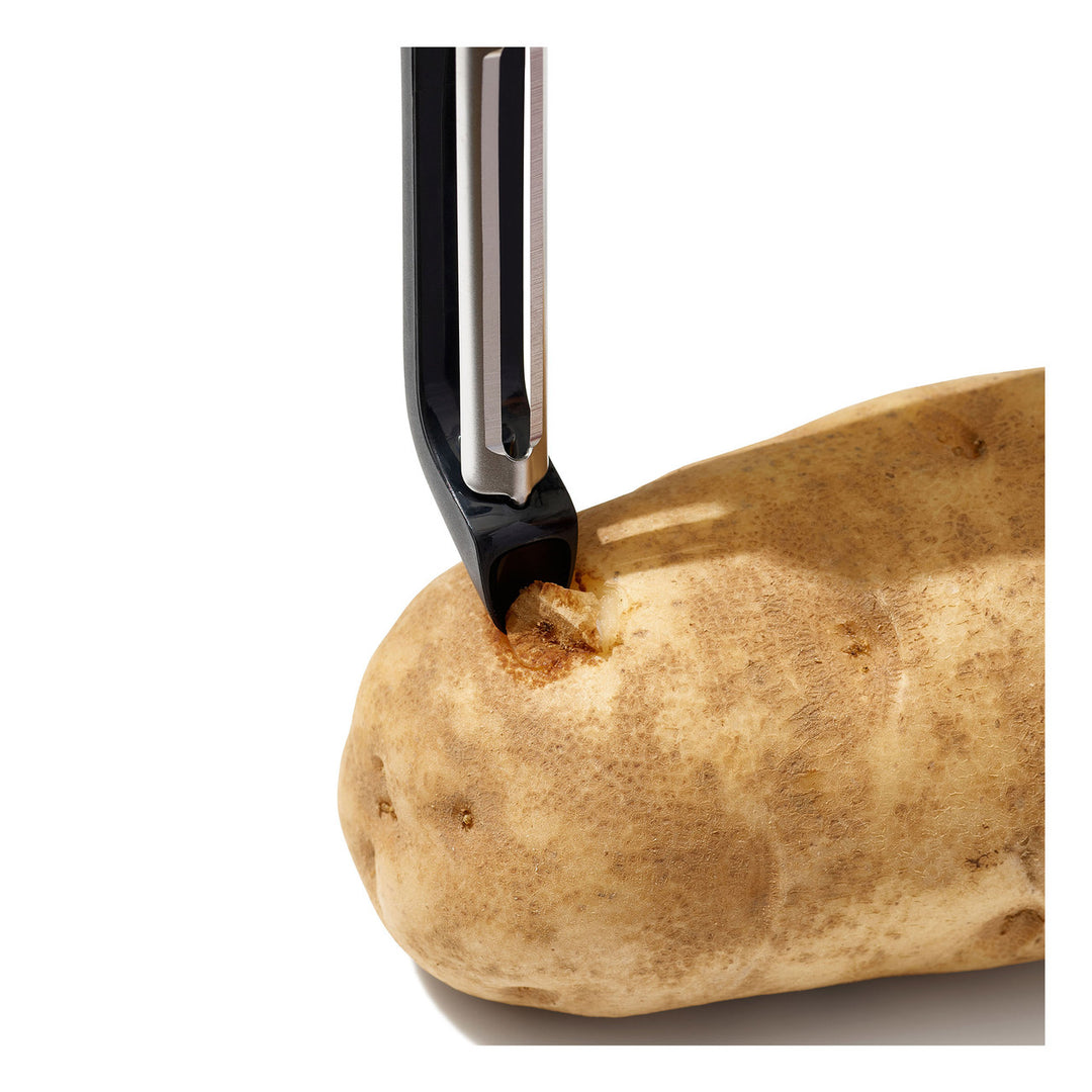 Black kitchen tool piercing a potato on a white background
