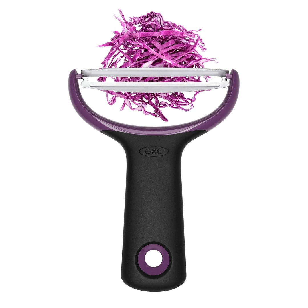 Purple and black vegetable peeler with pink shredded vegetables on a white background