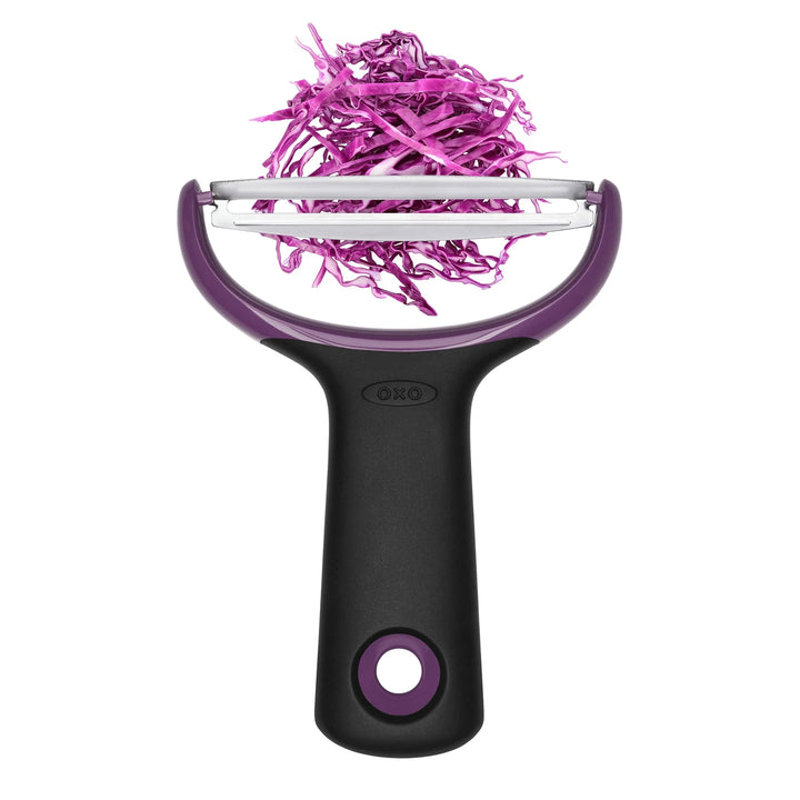 Purple and black vegetable peeler with pink shredded vegetables on a white background