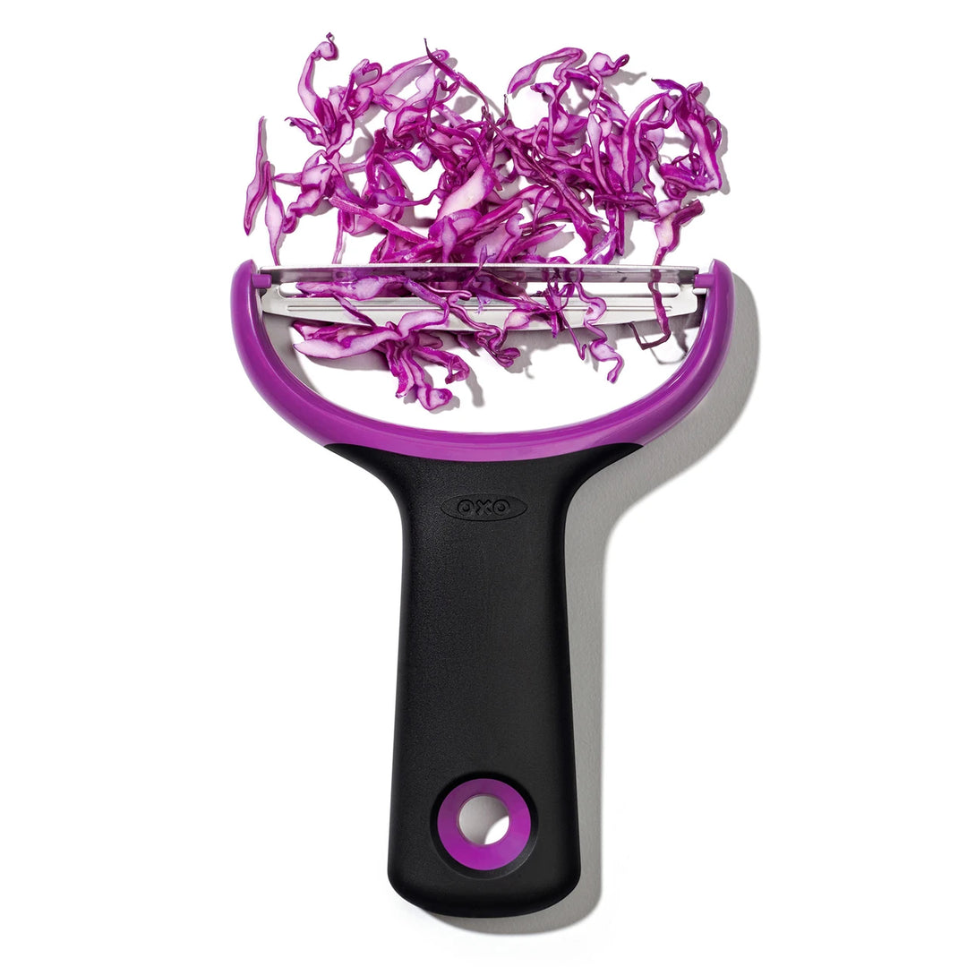 Purple and black vegetable peeler with sliced purple cabbage on a white background