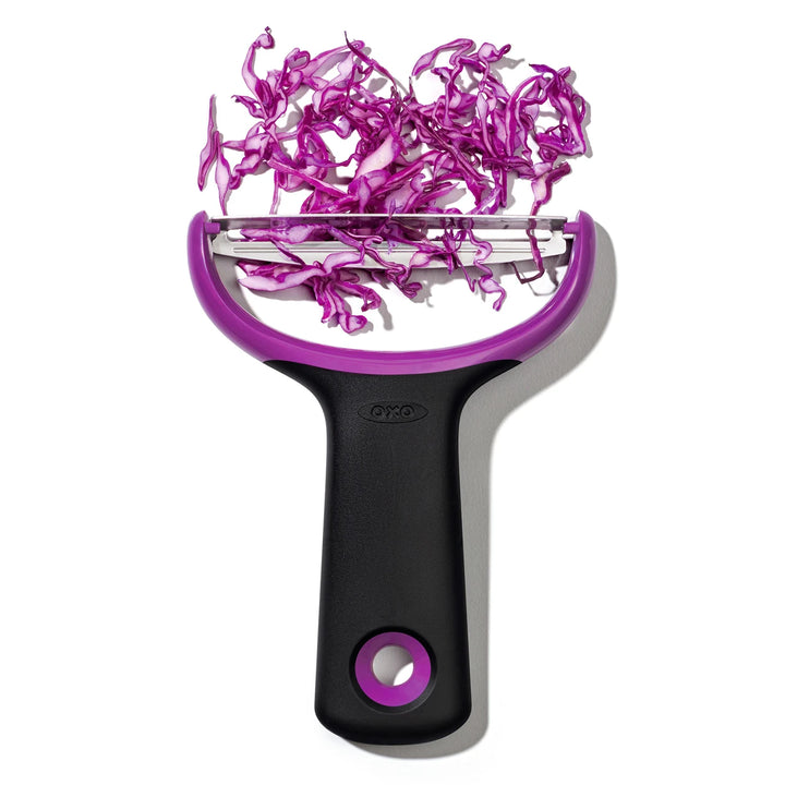 Purple and black vegetable peeler with sliced purple cabbage on a white background