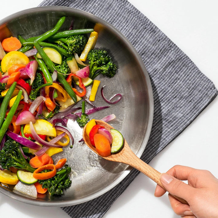 Colorful vegetables being stirred in a pan with a wooden spoon.