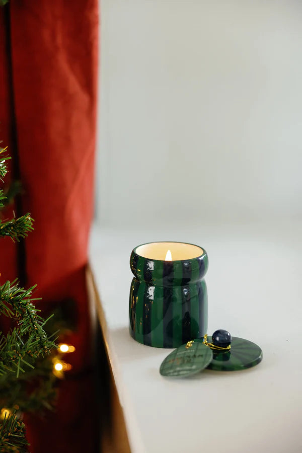 Green candle in a decorative holder on a white surface with a red curtain and Christmas tree in the background.