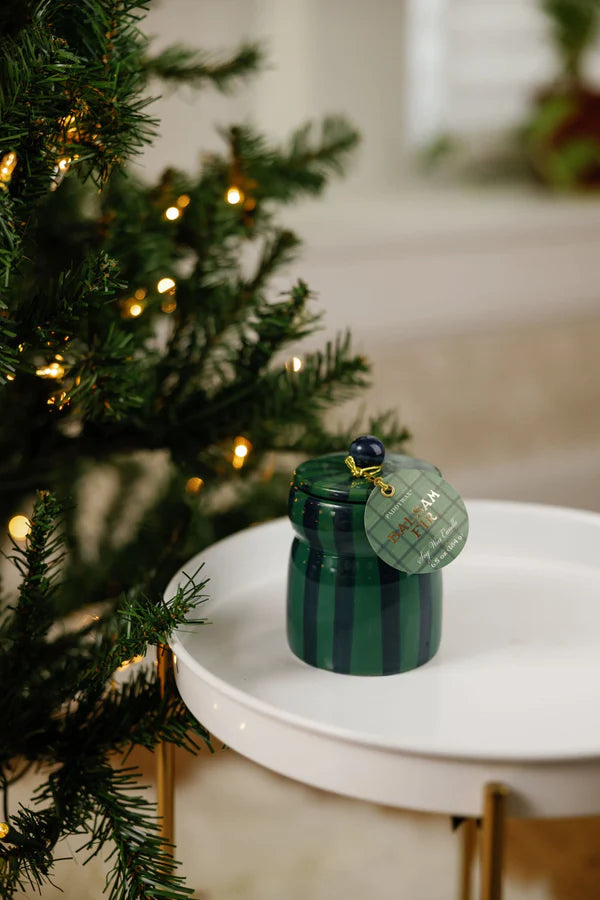 Green striped candle on a white surface next to a decorated Christmas tree