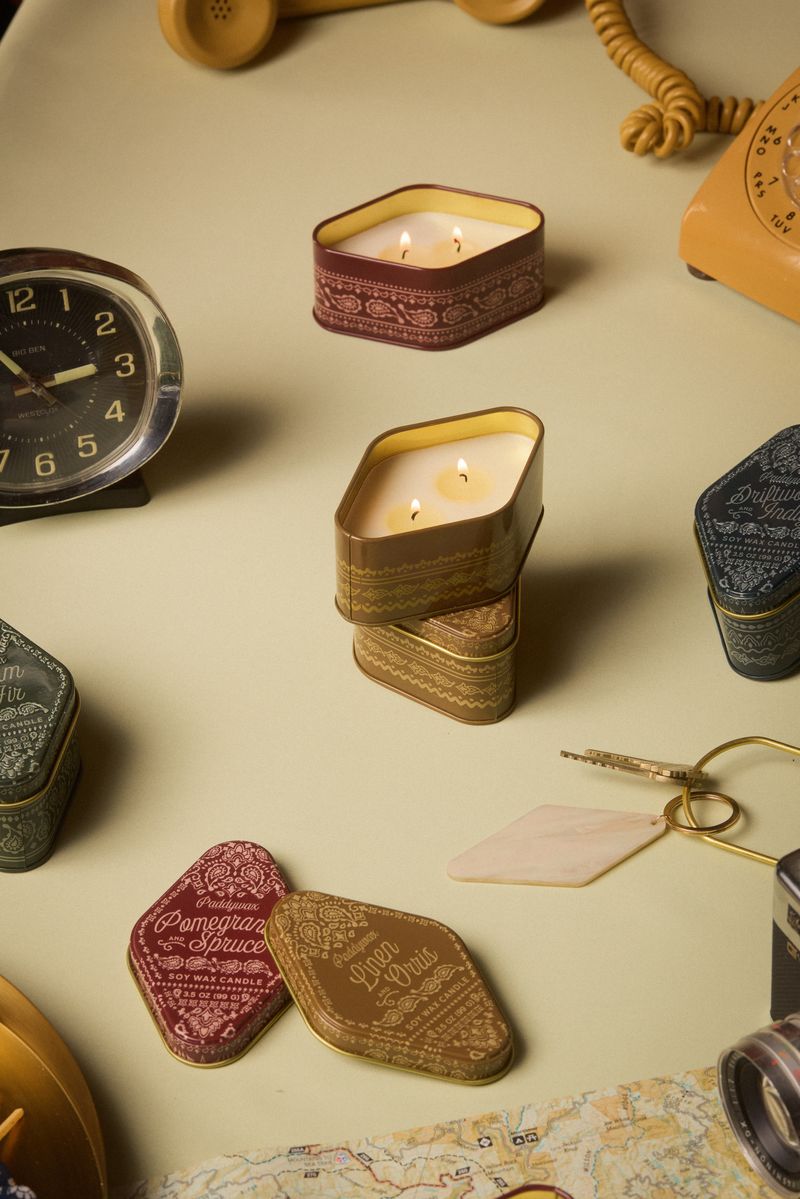 Candle in a decorative tin surrounded by vintage items on a light surface