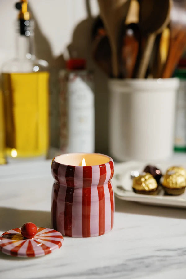 Striped candle in a kitchen setting with utensils and ingredients in the background