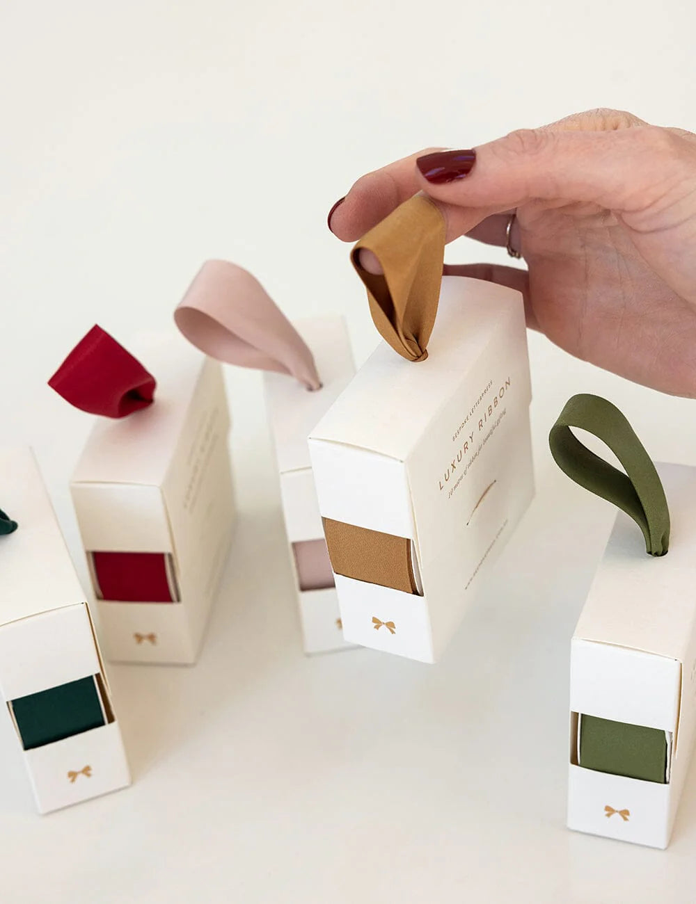 Hand holding a small fabric sample above a collection of white boxes with colorful fabric samples on a light background.
