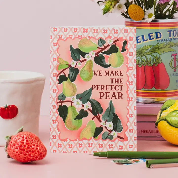 Card with pear design and text 'We make the perfect pear' on a pink background, surrounded by decorative items.