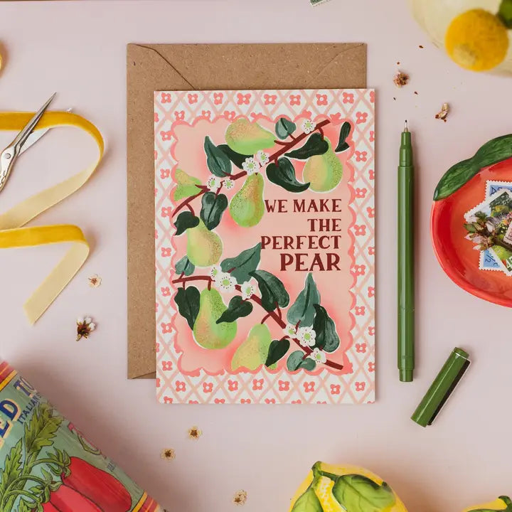 Greeting card with pear design and text 'WE MAKE THE PERFECT PEAR' on a decorative surface with stationery items.