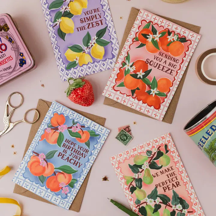 Collection of greeting cards with fruit illustrations on a table with stationery items.