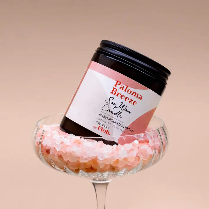 Jar of Paloma Breeze soy wax candle in a glass dish with pink and white decorative stones on a beige background