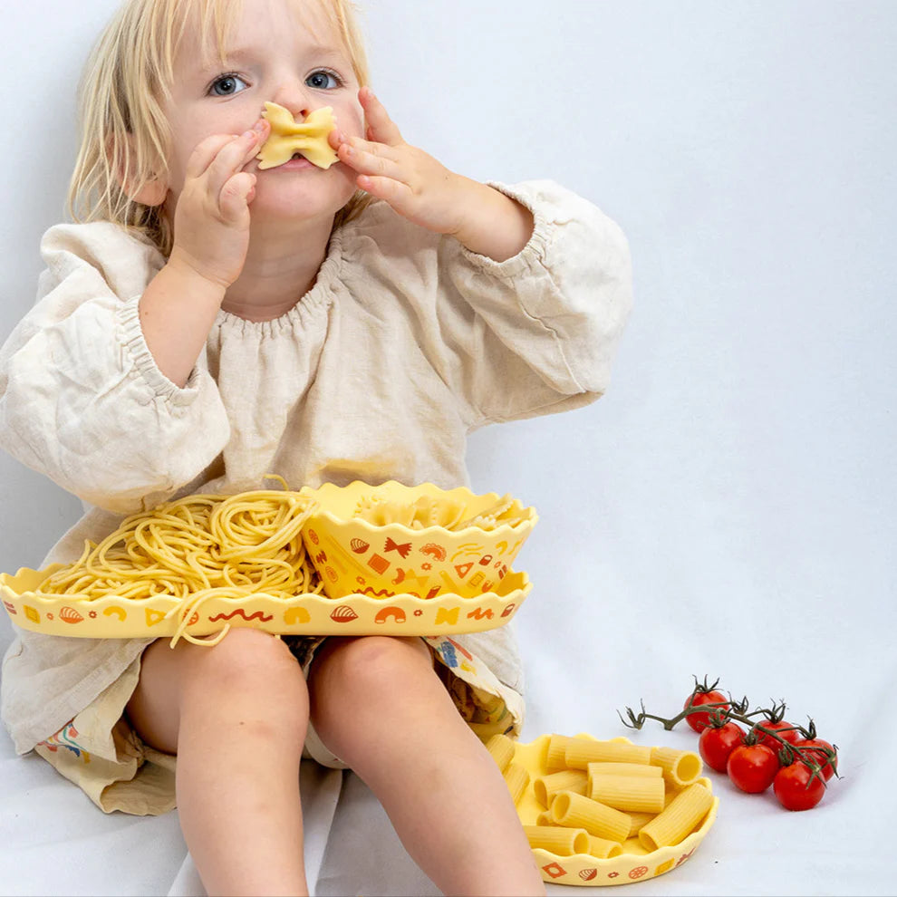 Child playing with pasta and vegetables on a white background