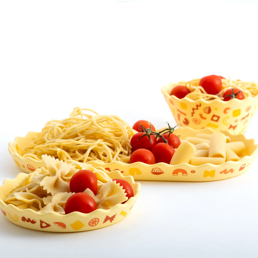 Three silicone pasta bowls with printed designs filled with pasta and tomatoes on a white background.