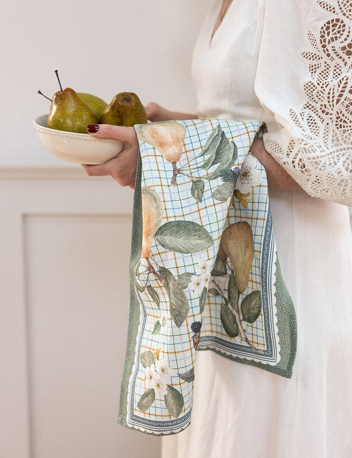 Person holding a bowl of pears with a decorative towel featuring fruit design.