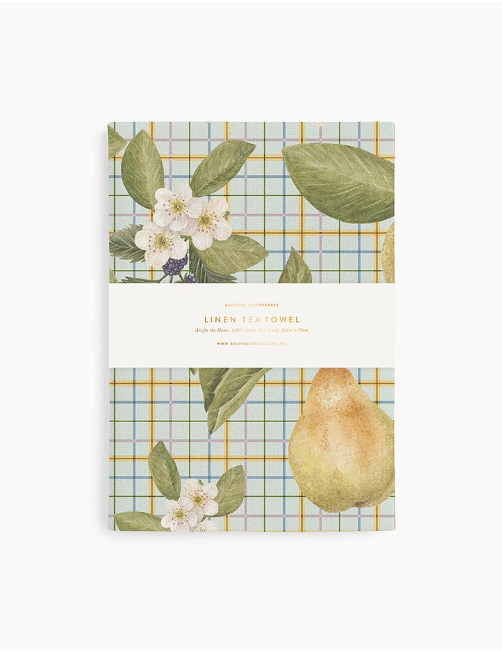 Packaging of a tea towel with plaid design and fruit illustration on a white background