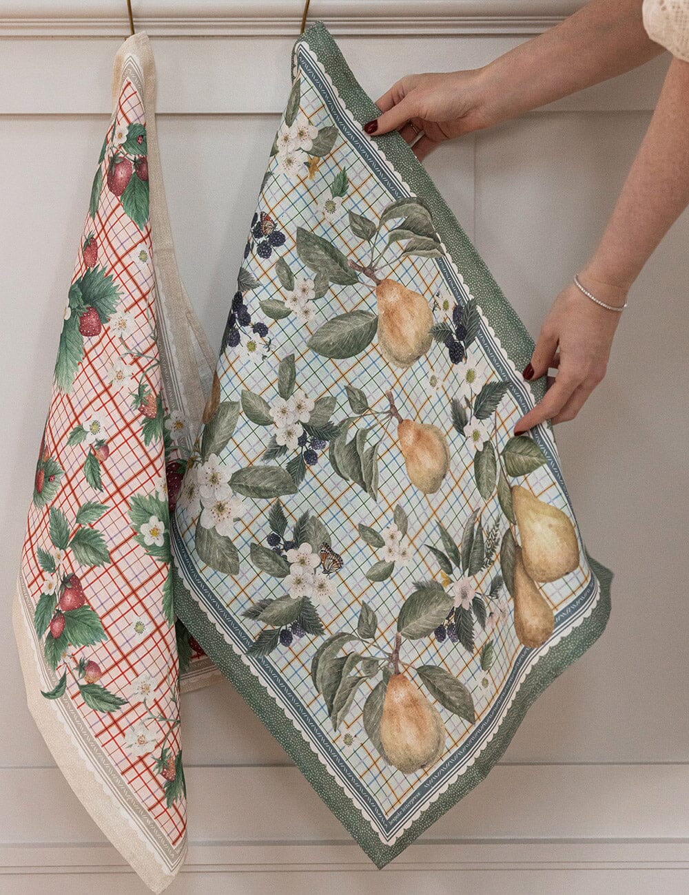 Two patterned towels hanging on a rack, one with plaid design and the other with fruit and floral design.