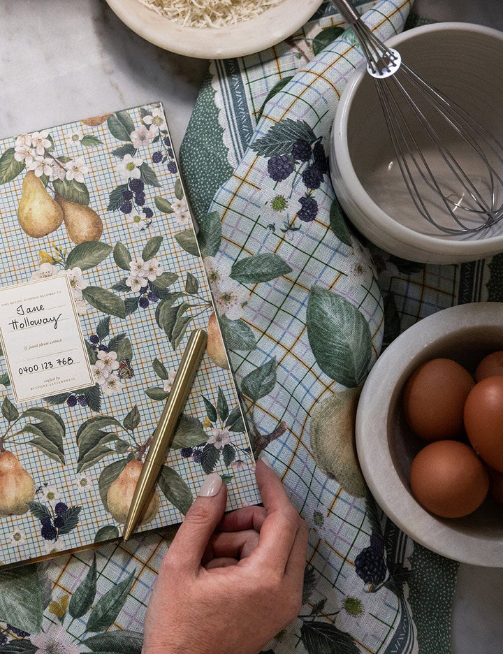 Notebook with floral design on a kitchen counter with eggs and a whisk.
