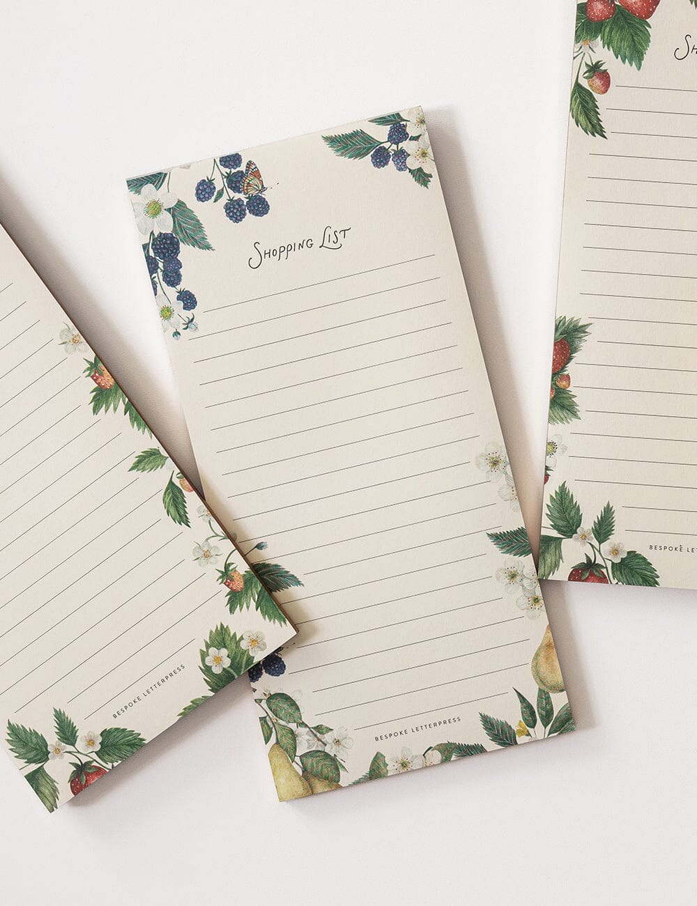 Set of three notepads with floral and fruit design on a white background