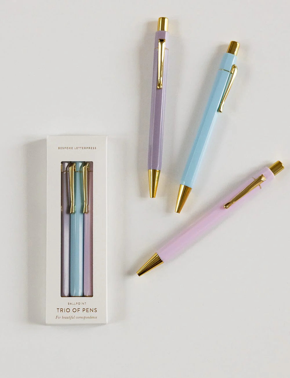 Three pastel-colored pens with gold accents on a white background, one pen outside its packaging.