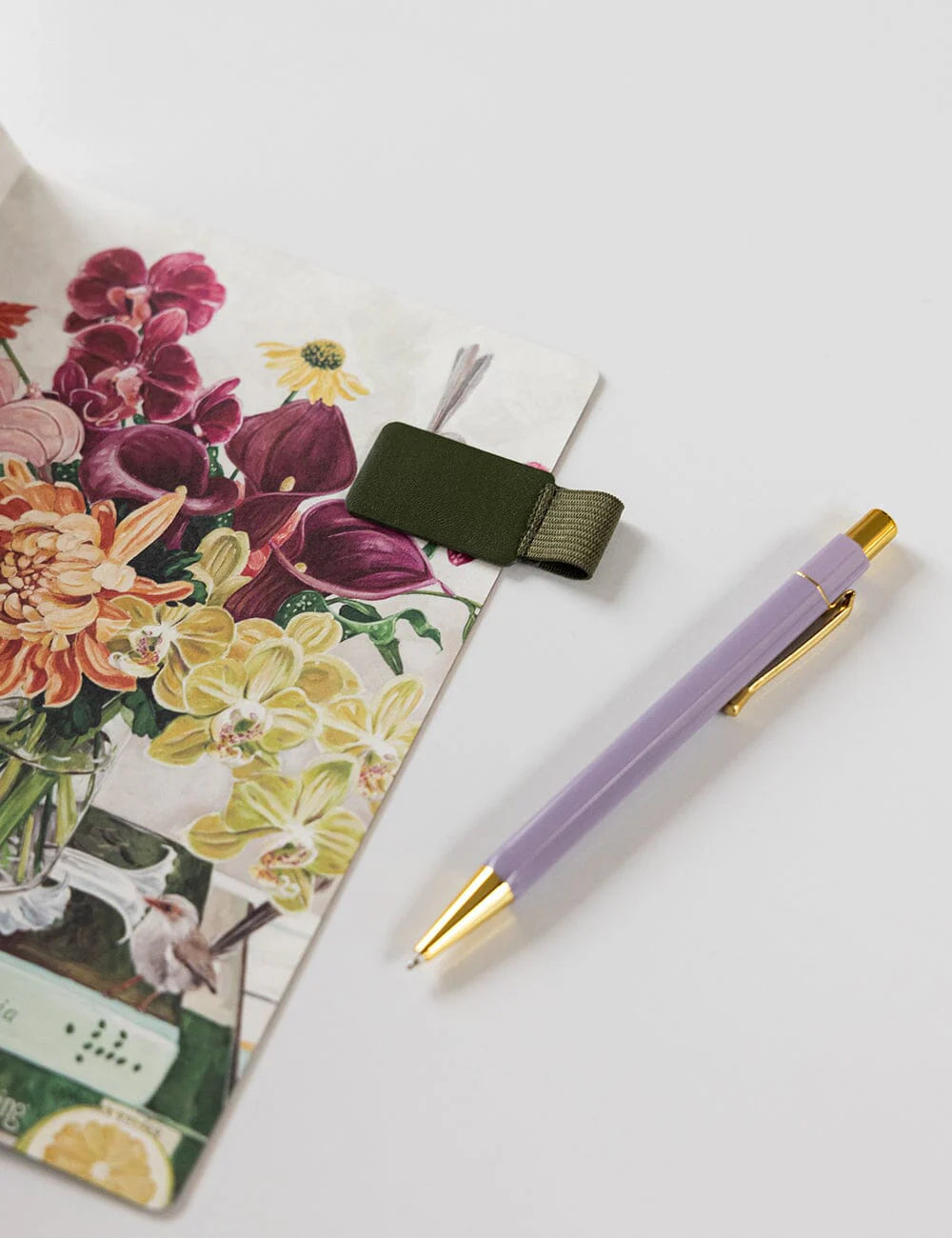 Purple pen with gold accents on a floral notebook and ribbon