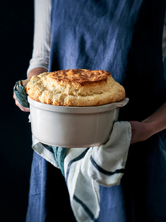 Person holding a dish with a baked dish, likely souffle, against a dark background