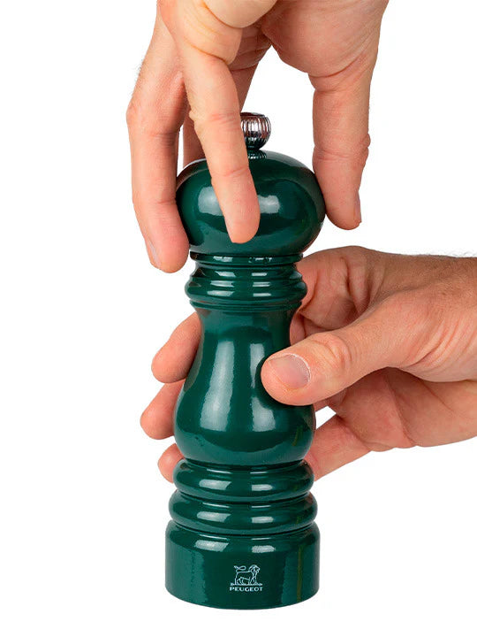 Green pepper grinder being held by a hand on a white background
