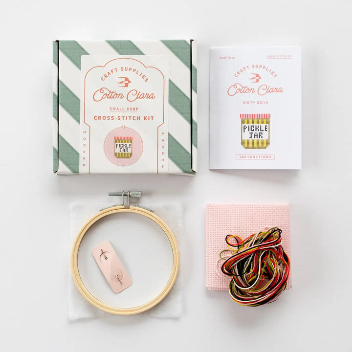 Cotton Clara craft supplies including a cross-stitch kit, embroidery hoop, and yarn on a white background.