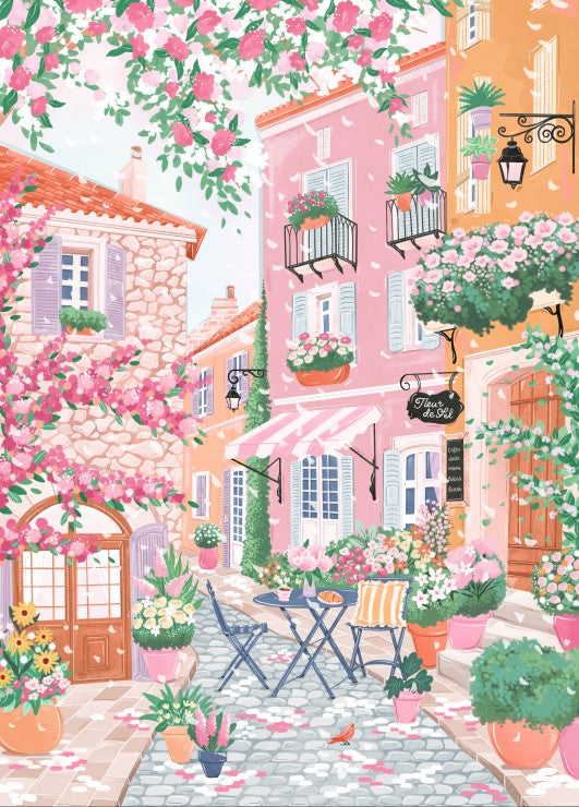 Colorful street scene with pink buildings, flowers, and a table with chairs.