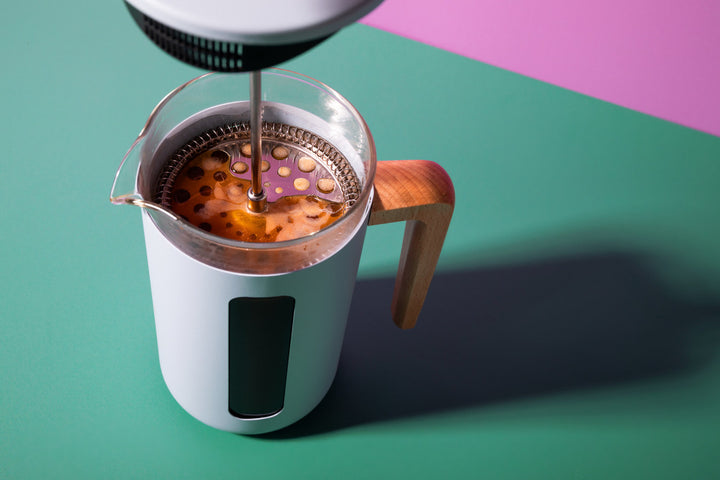 Coffee maker with a wooden handle on a green and pink background