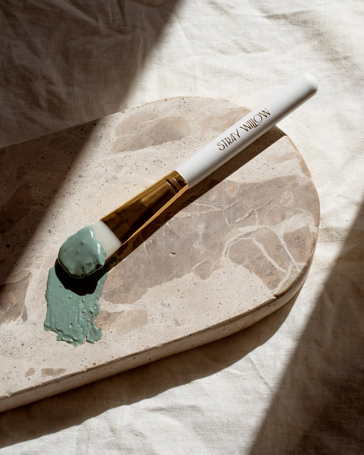 Paintbrush with green face mask on a marble surface