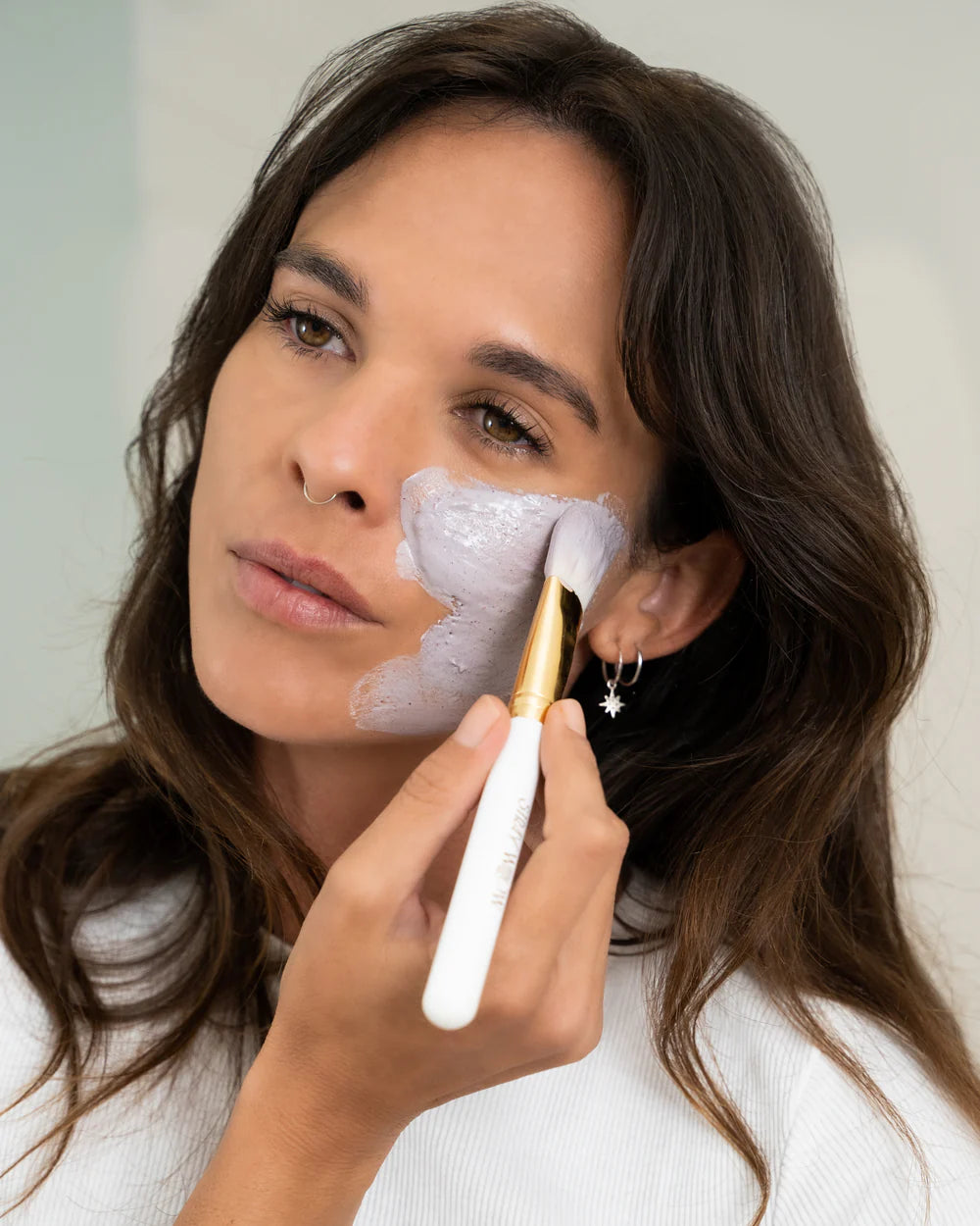 Woman applying a facial mask with a brush to her face.