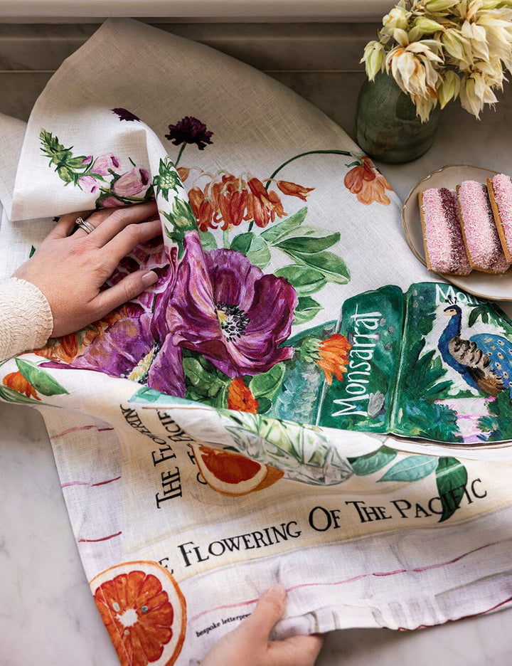 Floral-themed tea towel with a person holding it on a table.