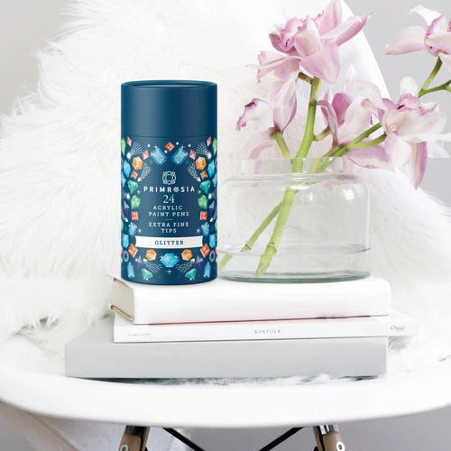 Blue cylindrical container with floral design on a white surface with pink flowers and books.