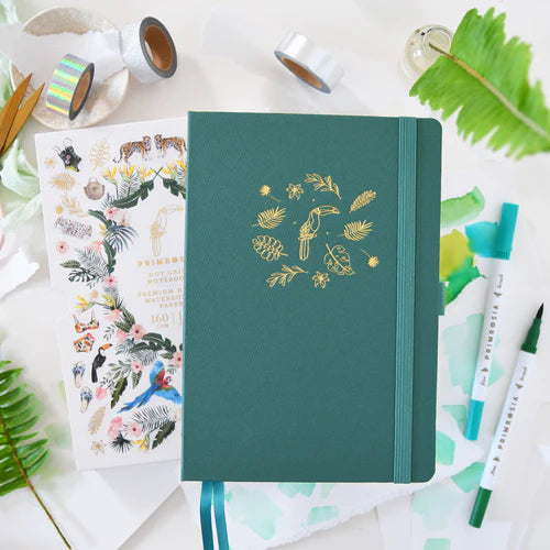 Green notebook with gold design on a white surface with stationery items