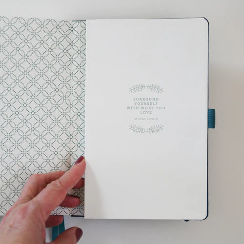 Hand holding a notebook with a decorative cover and text on a light background