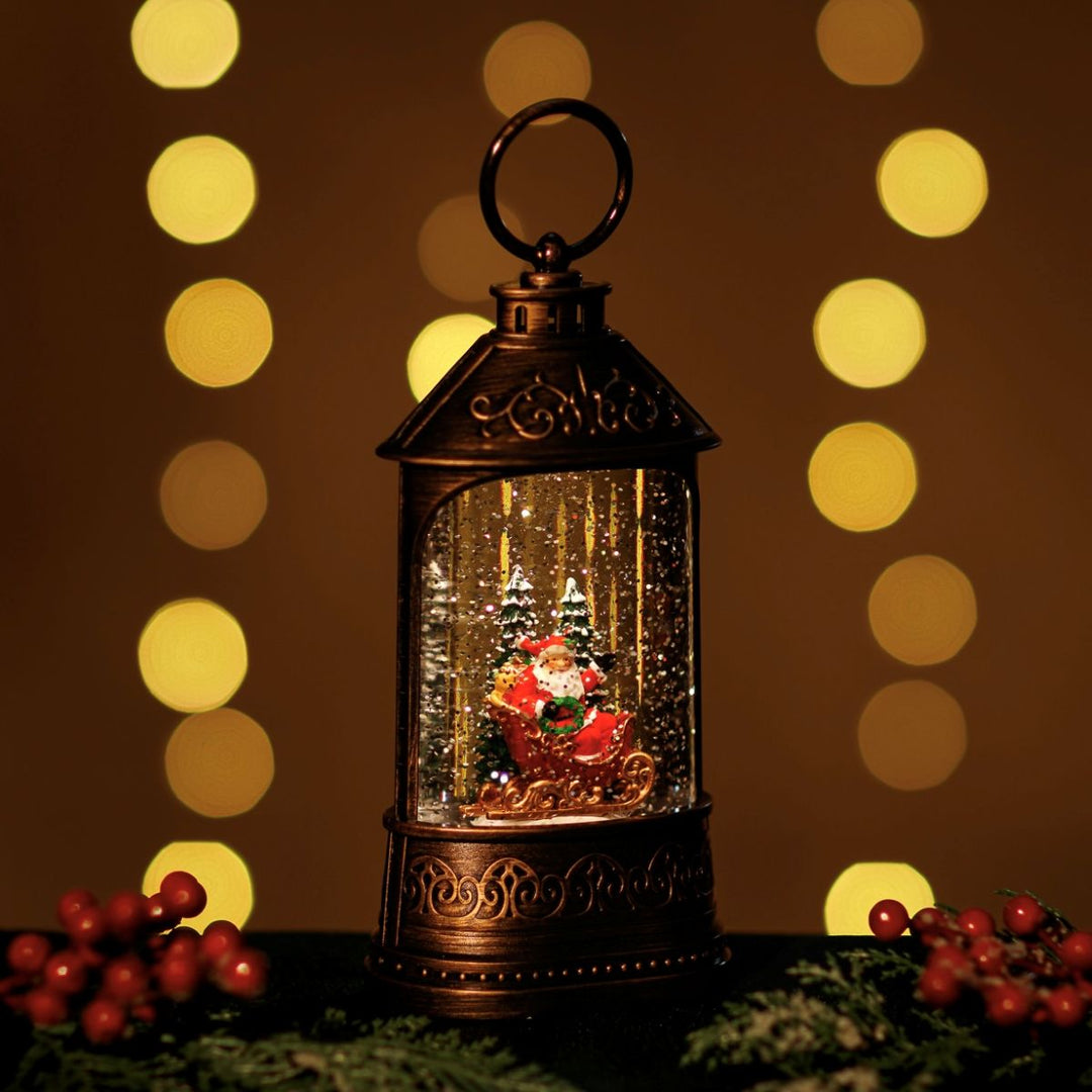 Decorative lantern with a Christmas scene inside, surrounded by blurred lights and foliage.