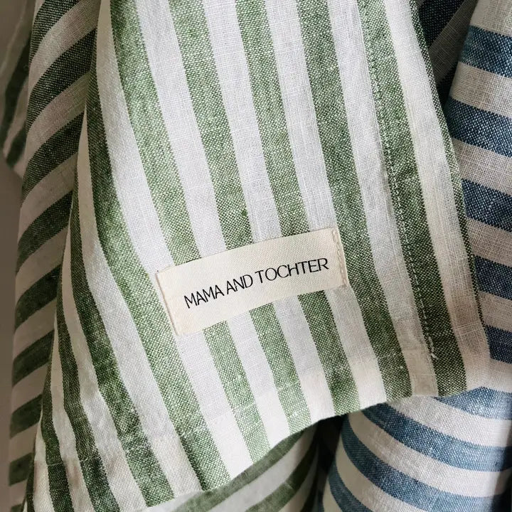 Close-up of a green and white striped linen tea towel with a 'MAMA AND TOCHTER' label.