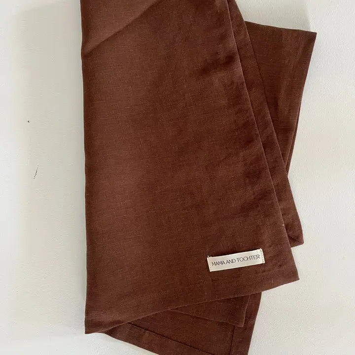 Brown linen tea towel with a visible brand label on a white background