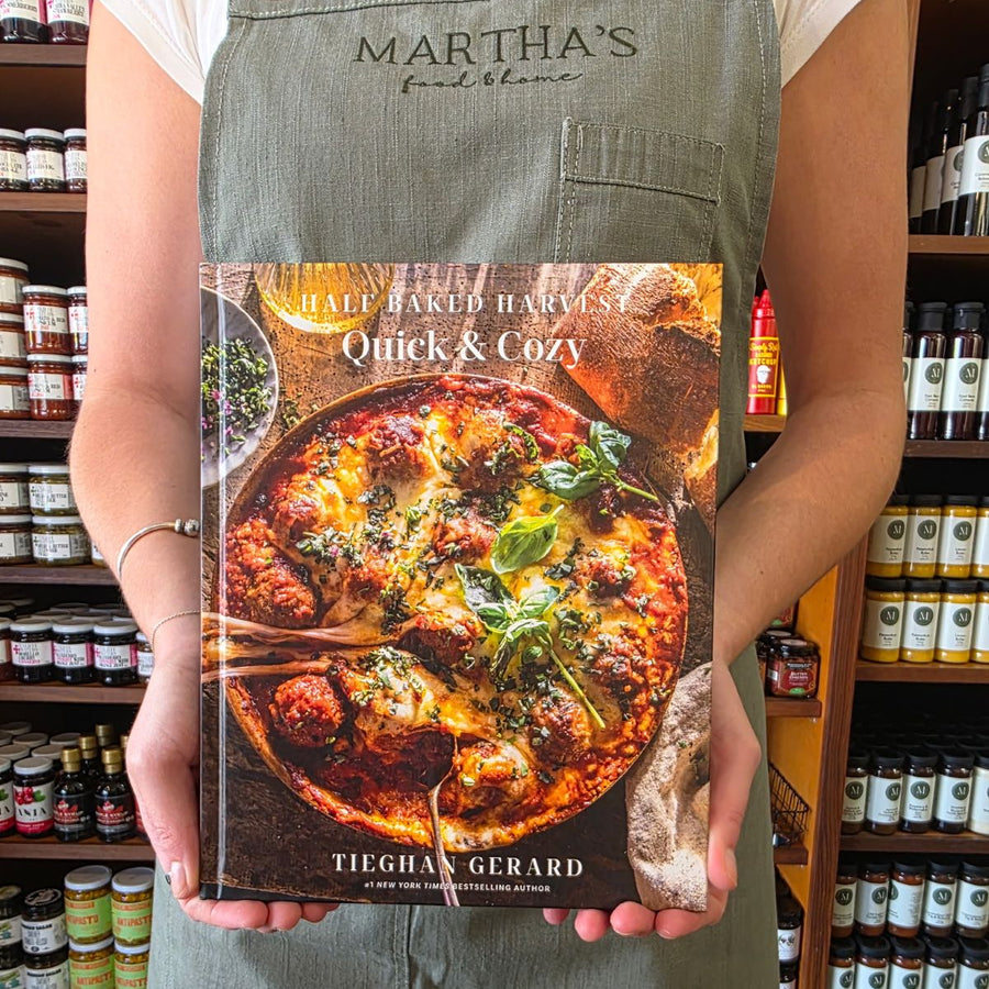 Person holding a cookbook titled 'Half Baked Harvest Quick & Cozy' in a store setting.